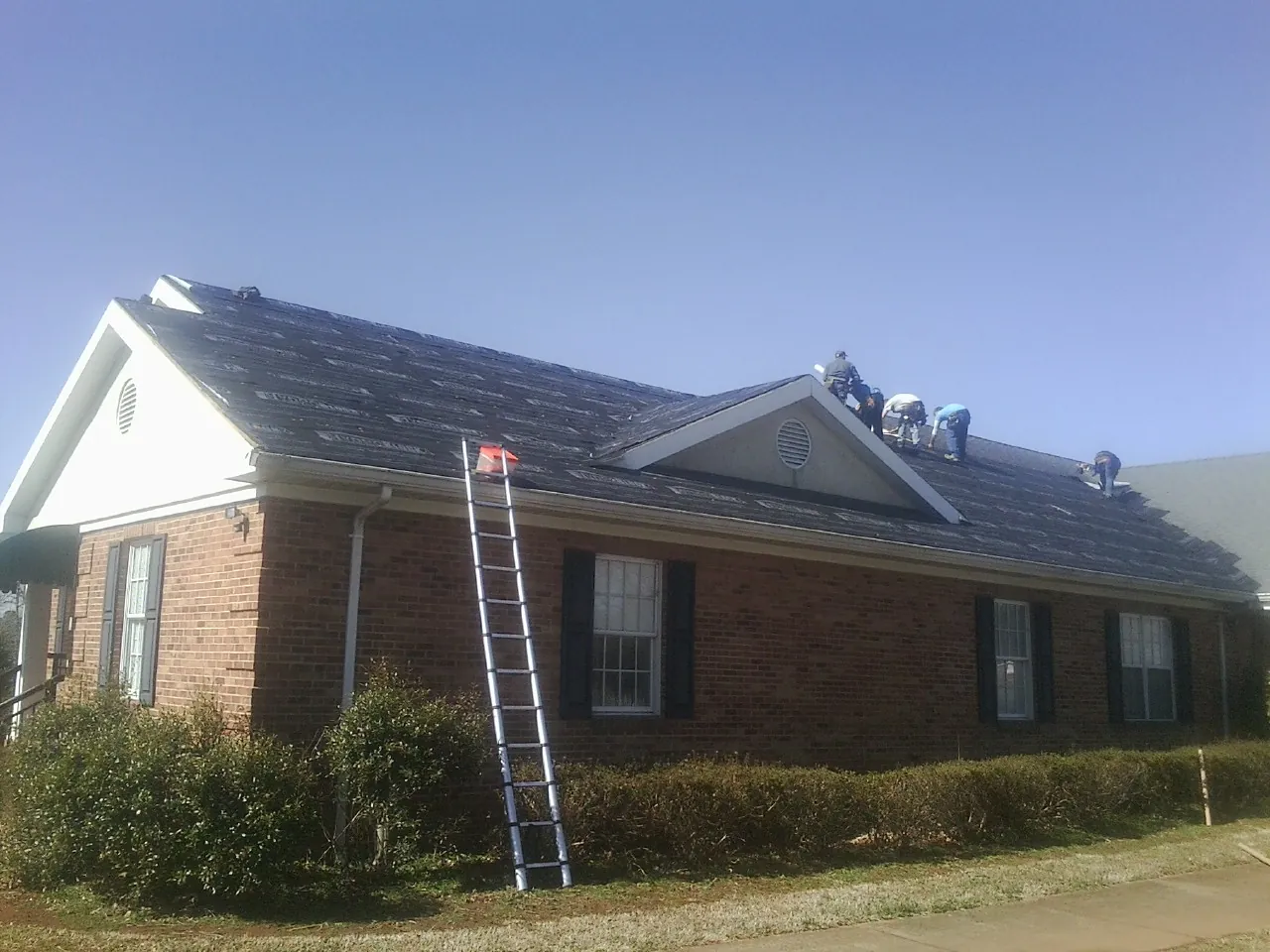 Crew tearing shingles off a brick ranch roof with a ladder set — Emergency Roof Repair work by our crew in Bethel