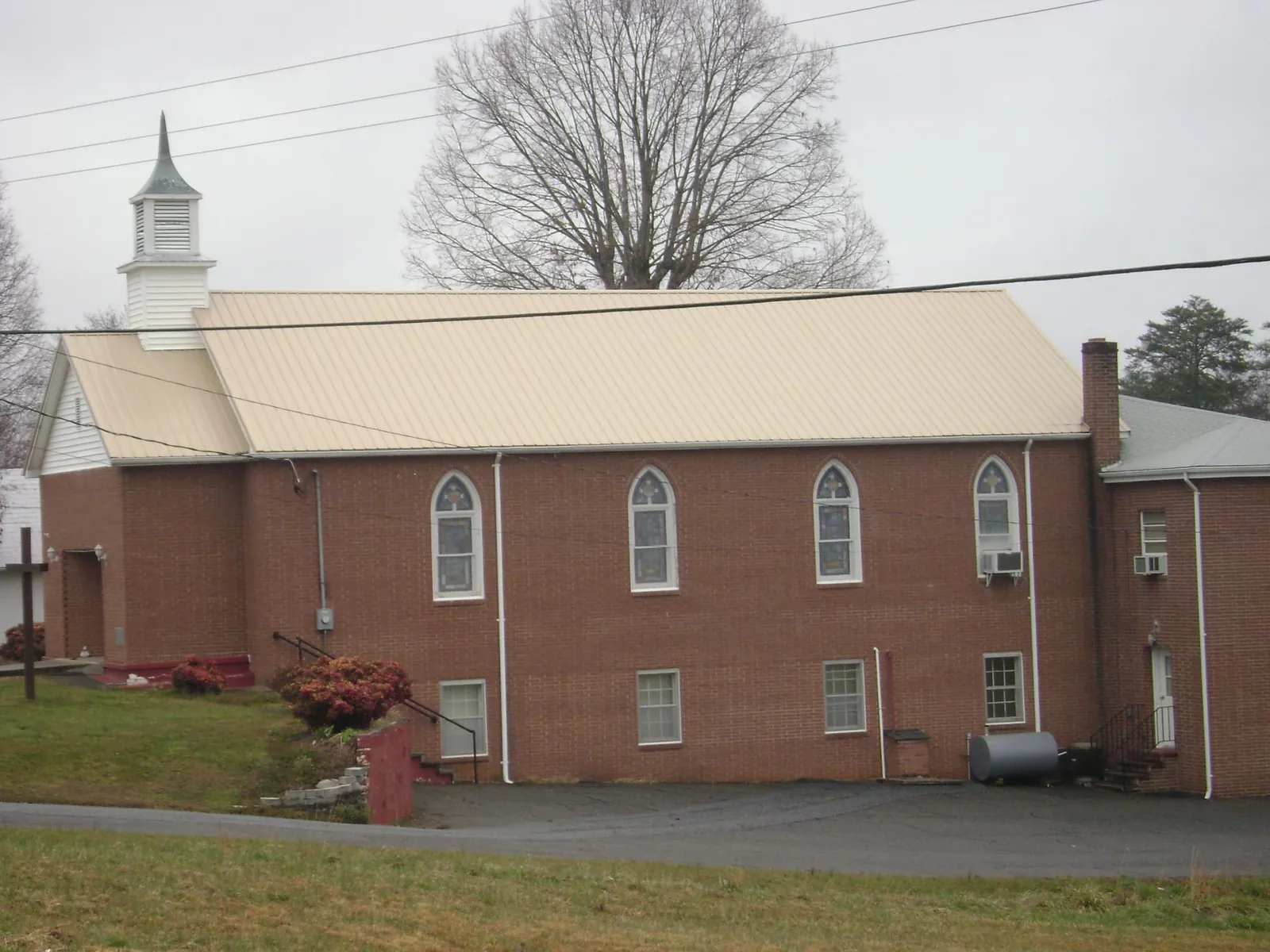 New tan metal roof on a brick church with a white steeple in Bethel