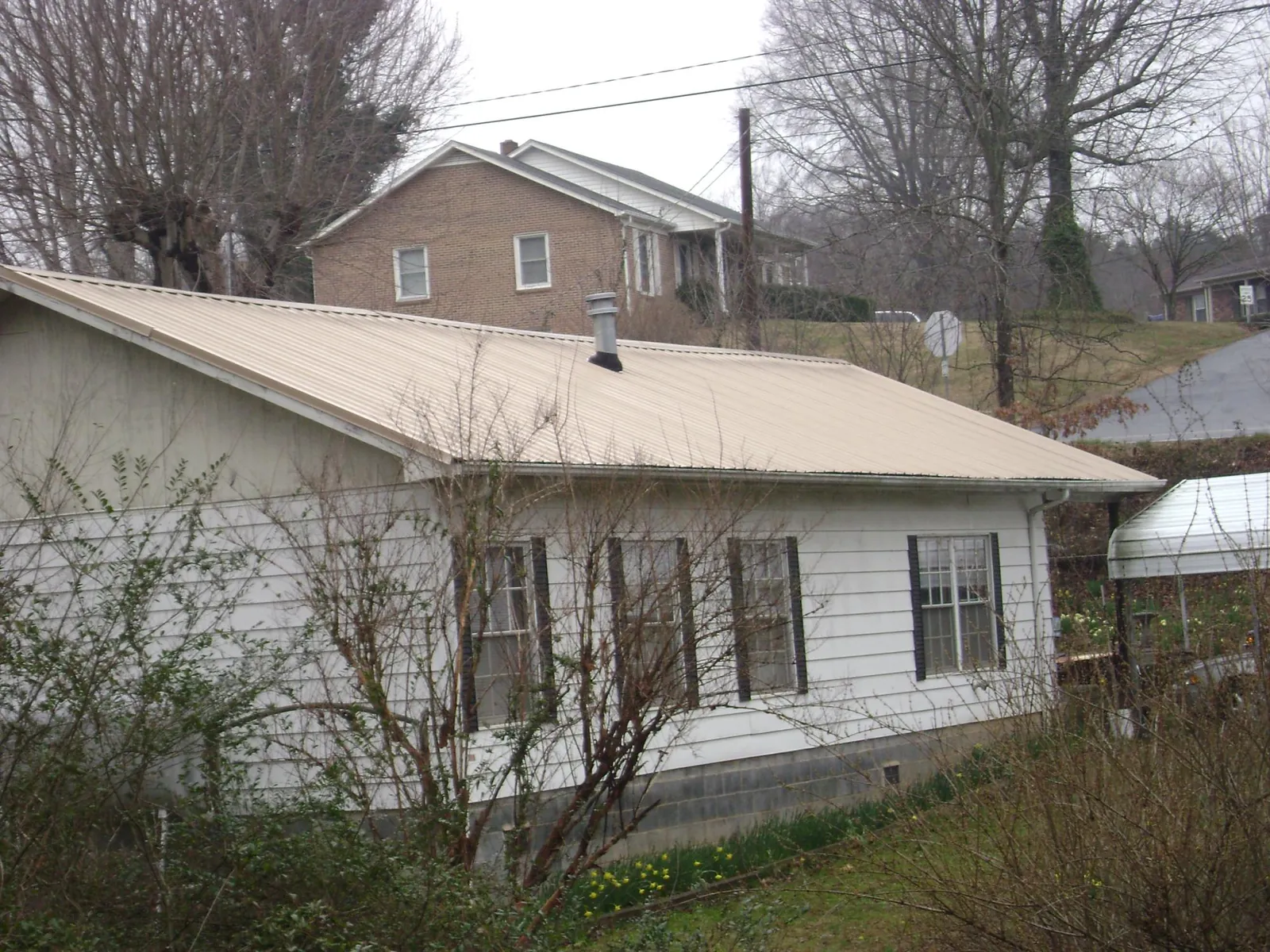 Tan metal roof on a white sided house set into a hillside — Commercial Roofing by Roofing Brothers in Bethel